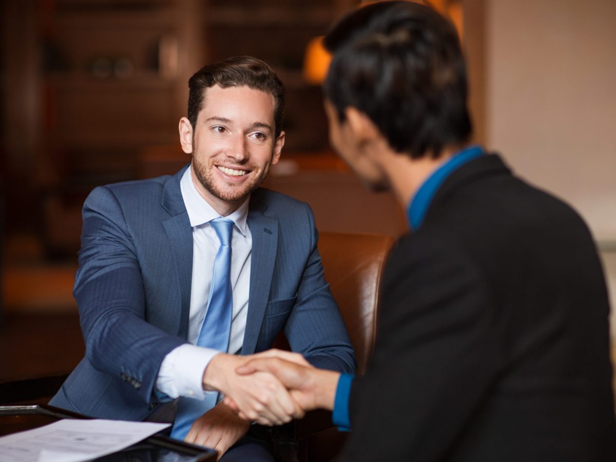 Closeup of two smiling business men shaking hands in cafe. One man is sitting back to camera.